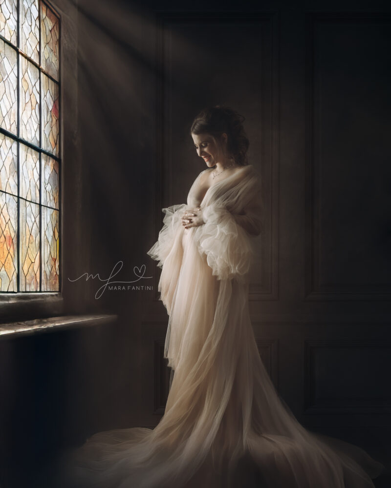 Ritratto fine art maternità a Roma in stile pittorico rinascimentale, donna con abito in tulle verde e sfondo ocra, fotografia d'autore di Mara Fantini.