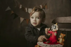 Bambino con pupazzo giocattolo durante un servizio fotografico Smash Cake a Roma, ambientazione calda con festoni decorativi