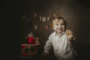 Bambino sorridente con un biscotto in mano durante un servizio fotografico Smash Cake a Roma, decorazioni dorate per il primo compleanno