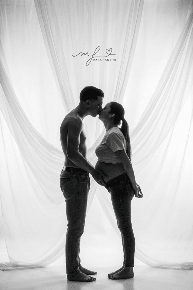 Foto di gravidanza artistica in bianco e nero in controluce, con un bacio intimo tra la futura mamma e il partner in uno studio fotografico a Roma.