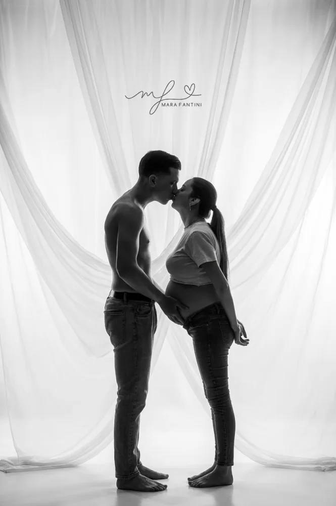 fotografia-maternita-artistica-controluce-roma.jpg Foto di gravidanza artistica in bianco e nero in controluce, con un bacio intimo tra la futura mamma e il partner in uno studio fotografico a Roma.