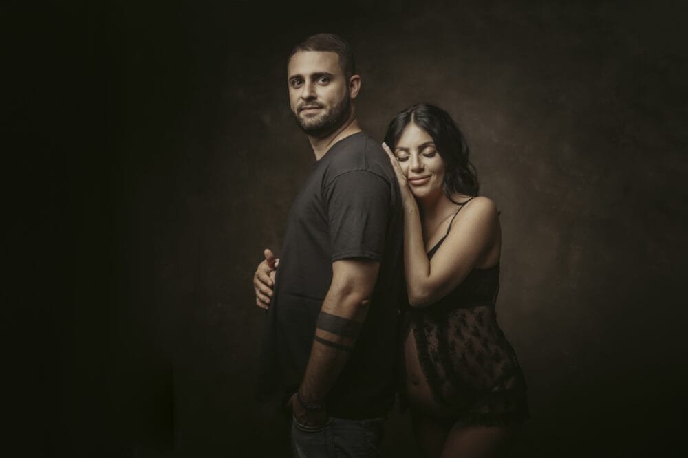 Fotografa gravidanza Roma — coppia in studio, luce calda, momento naturale senza posa