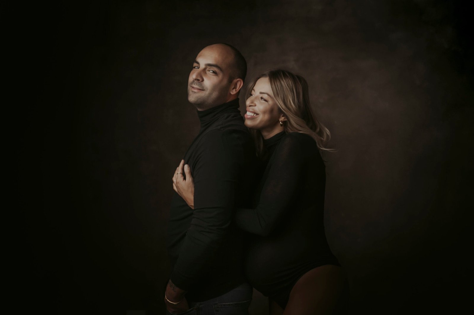 Fotografa gravidanza Roma — coppia abbracciata in studio, tono caldo, sguardo complice