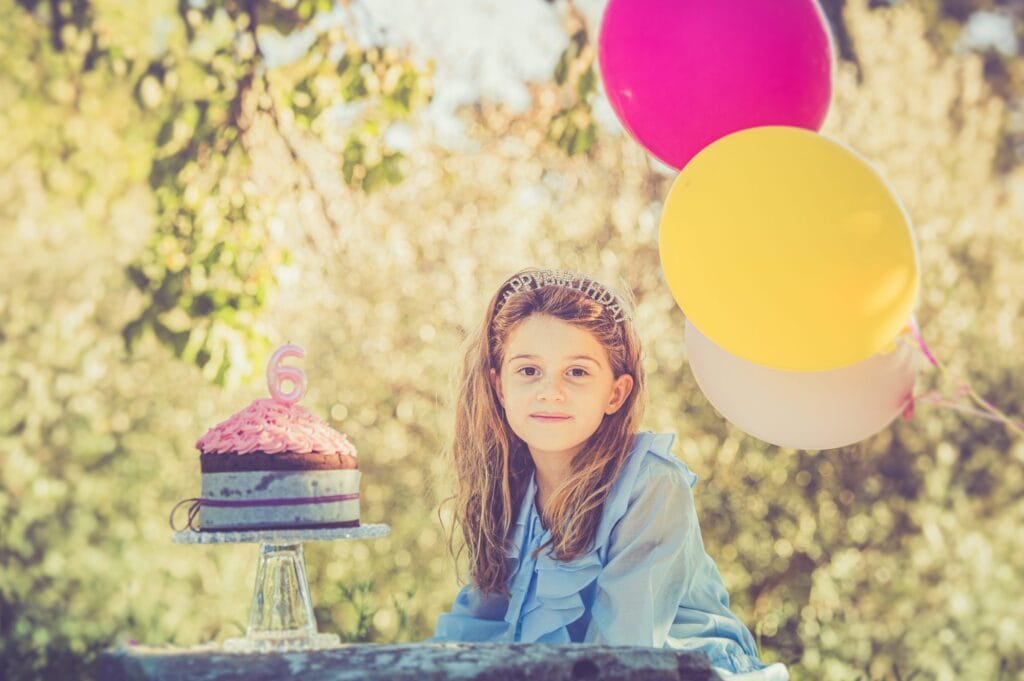 Bambina di sei anni sorride accanto alla torta di compleanno con candelina a forma di 6 e palloncini colorati, Parco degli Acquedotti Roma