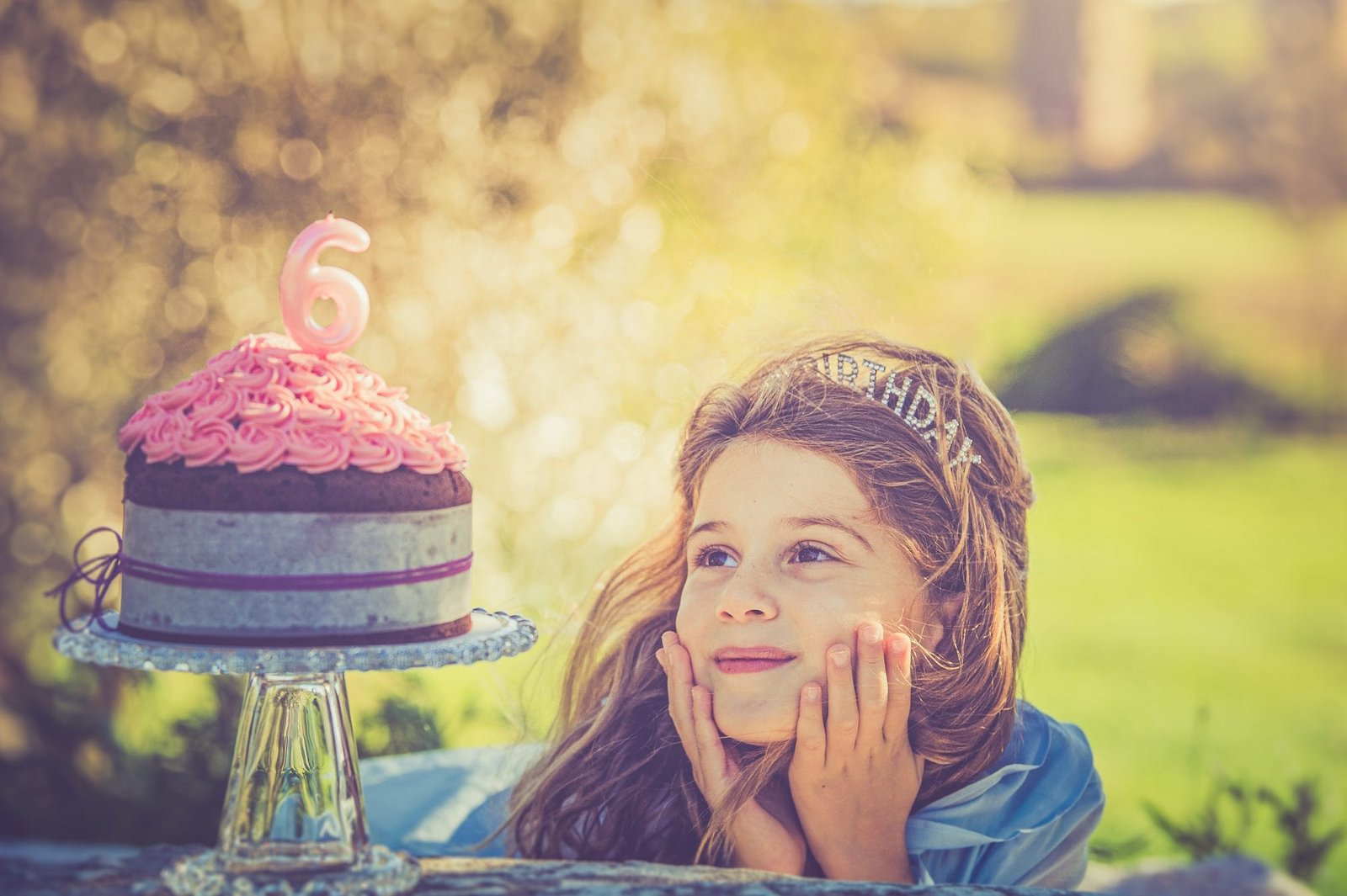 Bambina appoggia il viso sulle mani con sguardo sognante verso la torta di compleanno, servizio fotografico di famiglia a Roma
