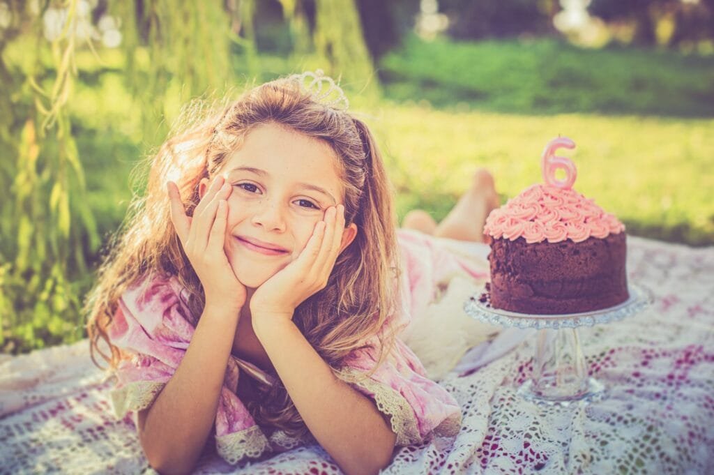 Bambina sdraiata su un plaid sotto un salice piangente, torta di compleanno sullo sfondo, Parco degli Acquedotti
