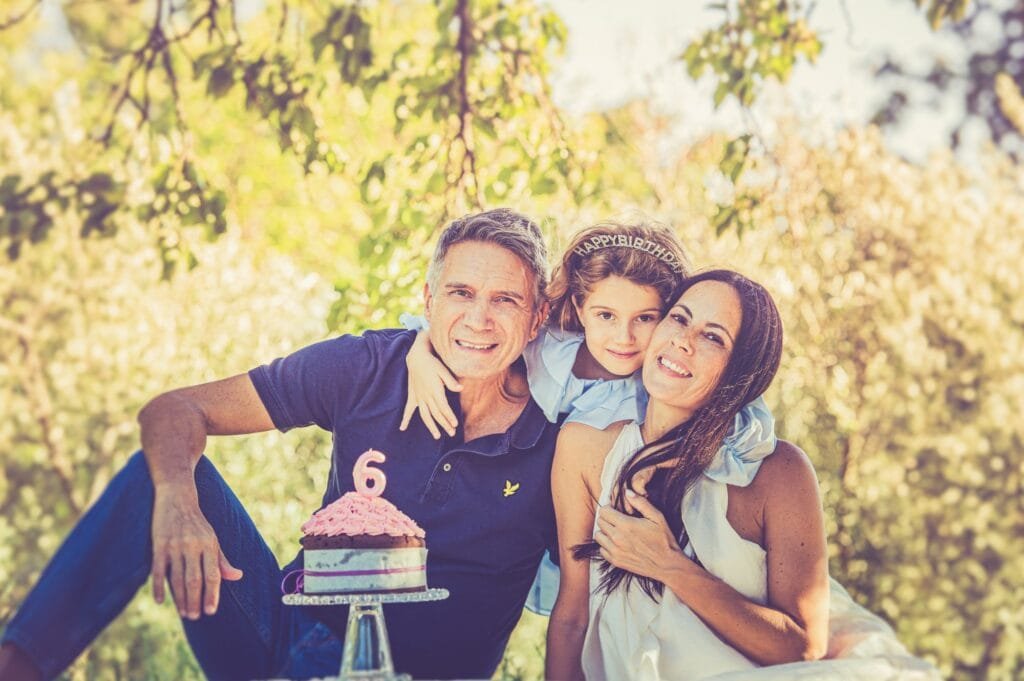 Ritratto di famiglia abbracciata e sorridente, torta con candelina a forma di 6 in primo piano